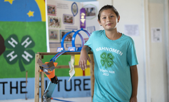 A girl wearing a 4-H shirt standing next to her 4-H exhibit.